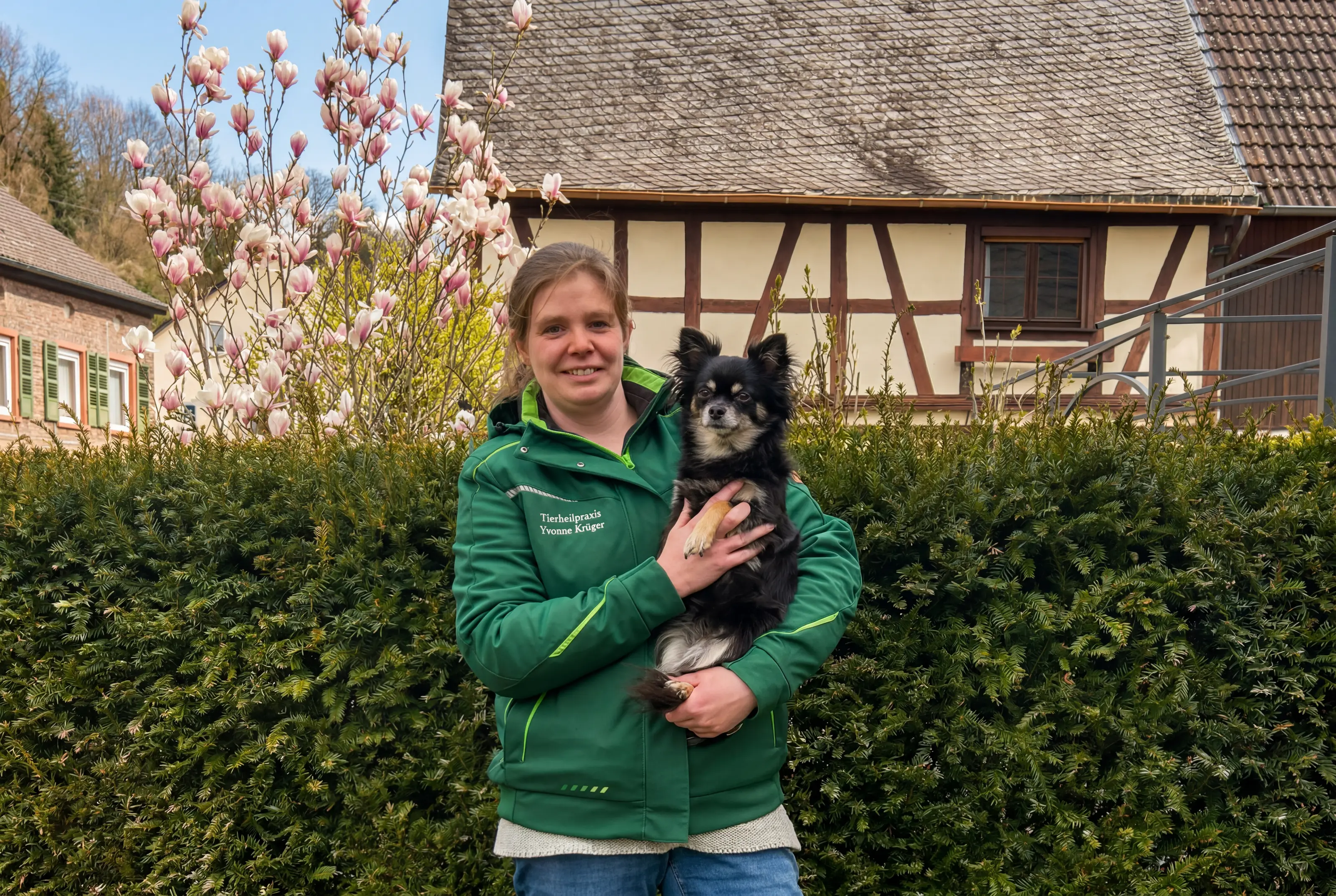 Yvonne Krüger mit einem kleinen schwarzen Hund auf dem Arm vor einem Fachwerkhaus