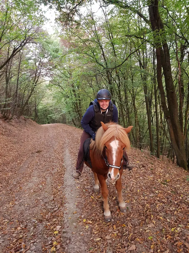 Yvonne Krüger reitet auf ihrem Pferd einen Waldweg entlang